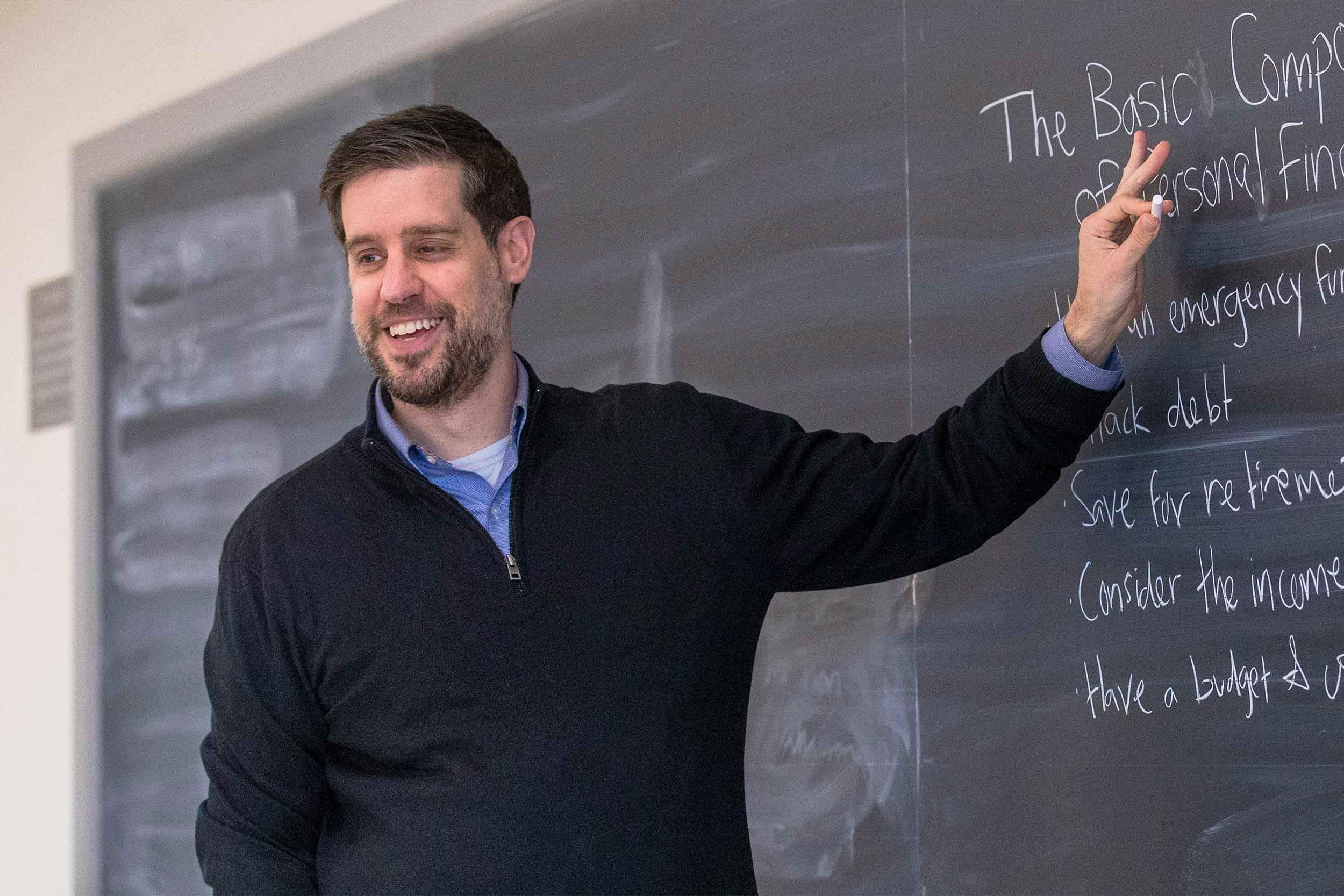 Professor Andrew Pennock smiling in front of a class while at the chalkboard