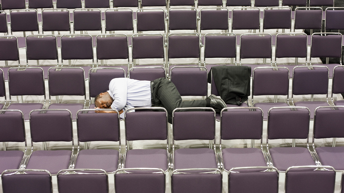 Man in business suit laying on a bunch of empty chairs