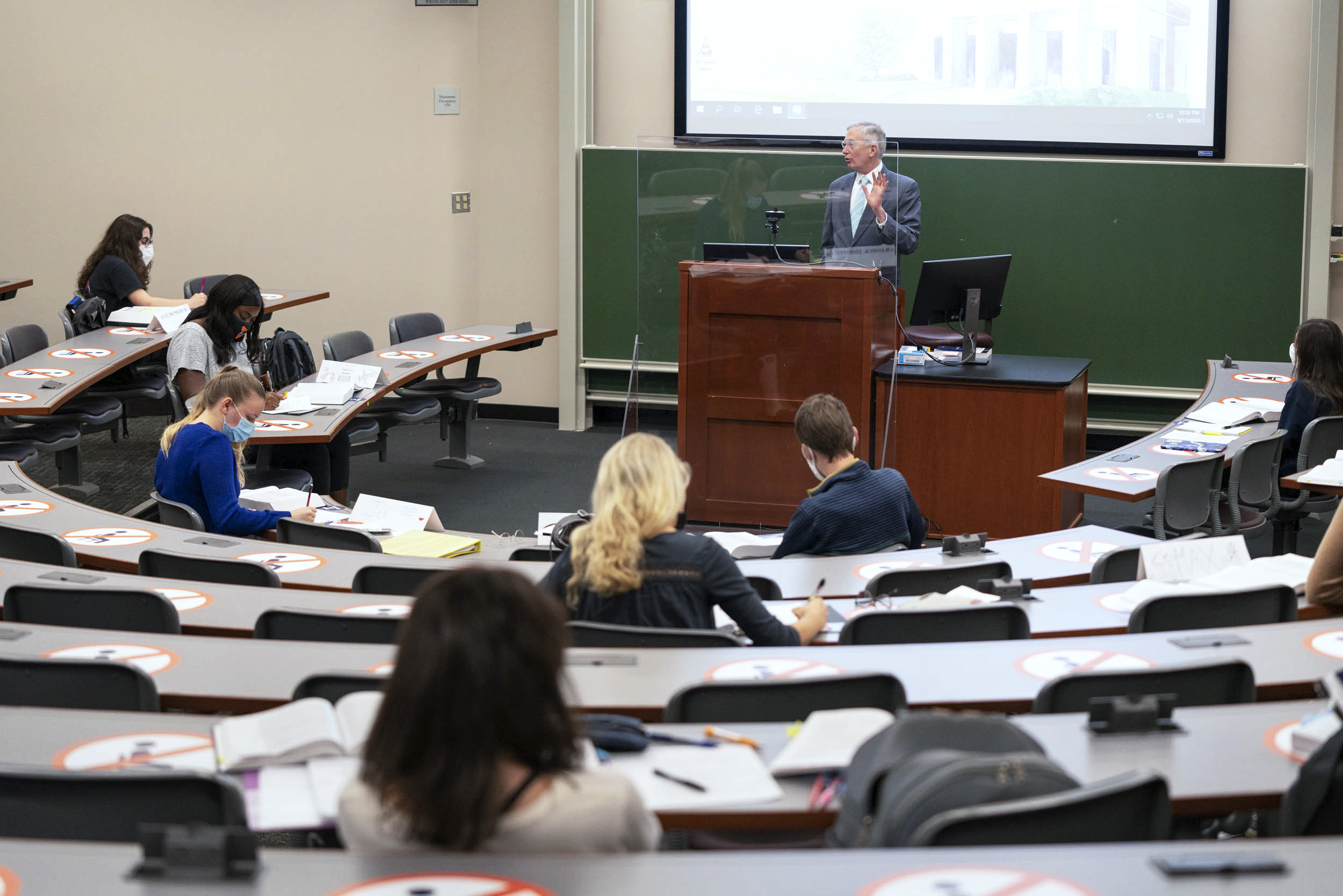 In School of Law professor Paul Mahoney's class, each seat is marked for physical distancing and Mahoney teaches behind a clear plastic shield, with a portion of the students attending in person and the remainder viewing the lecture synchronously online.