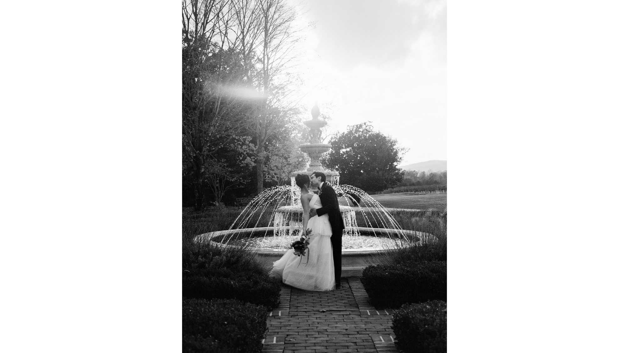 Black and white wedding photo of Michael Pugh kissing his wife and fellow Batten student in front of a fountain