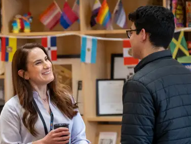 Two people talking, one smiling, with multicultural flags in the background